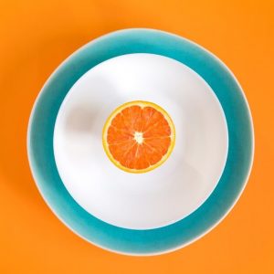 Cut orange piece on a white plate on an orange background