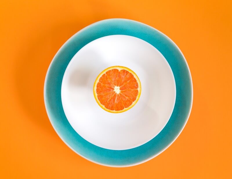 Cut orange piece on a white plate on an orange background