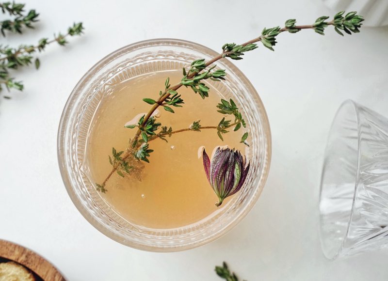 Brown liquid in a bowl with a sprig of rosemary