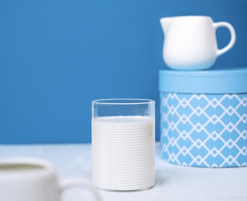 Glass with milk and a small white jug on blue background