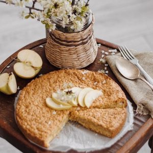 Apple pie with slices of the fruit and a basket of wild flowers in rustic settings.